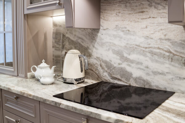 Gray and white stone backsplash from Youngstown Granite & Quartz behind a stovetop in a kitchen.