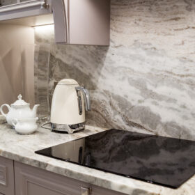 Gray and white stone backsplash from Youngstown Granite & Quartz behind a stovetop in a kitchen.